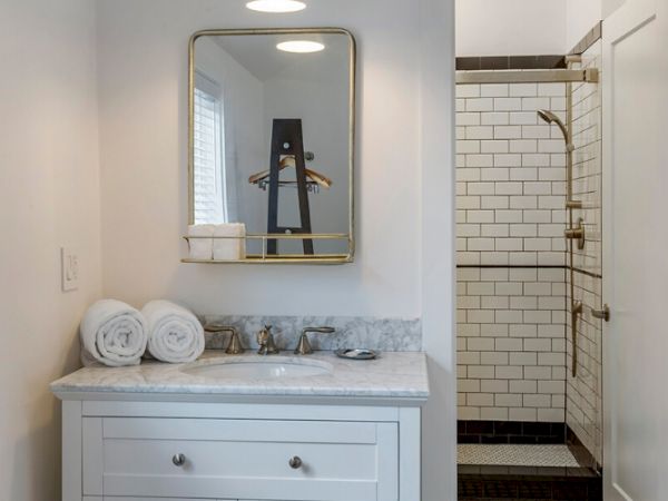 The image shows a bathroom with a marble-topped vanity, a mirror, rolled towels, a window, and a shower with white subway tiles.