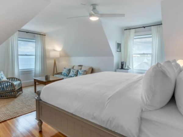A cozy bedroom with a bed, sofa, coffee table, TV, and windows with curtains. The room has a bright and airy atmosphere.