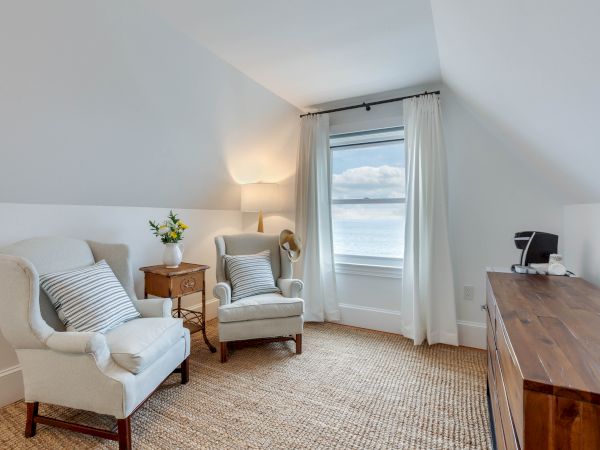 A cozy room with two armchairs, a lamp, a wooden dresser, and a window with a view. Neutral tones create a calm atmosphere.