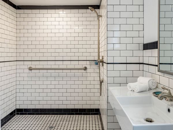 The image shows a bathroom with white subway tiles, a shower, a sink with a mirror, and a towel rack.