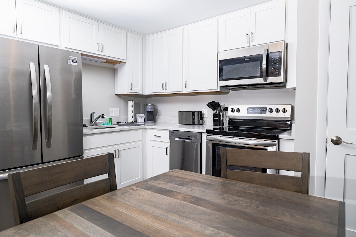 A modern kitchen with white cabinets, stainless steel appliances, and a wooden table and chairs in the foreground.