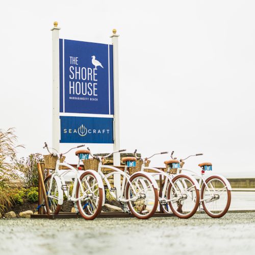 The image shows a row of vintage-style bicycles parked near a sign for "The Shore House" and "Sea Craft."