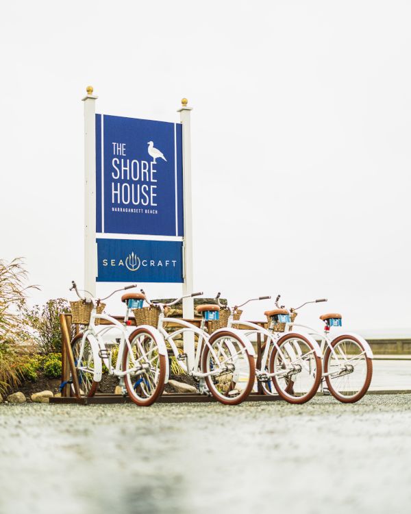 The image shows a row of vintage-style bicycles parked near a sign for "The Shore House" and "Sea Craft."