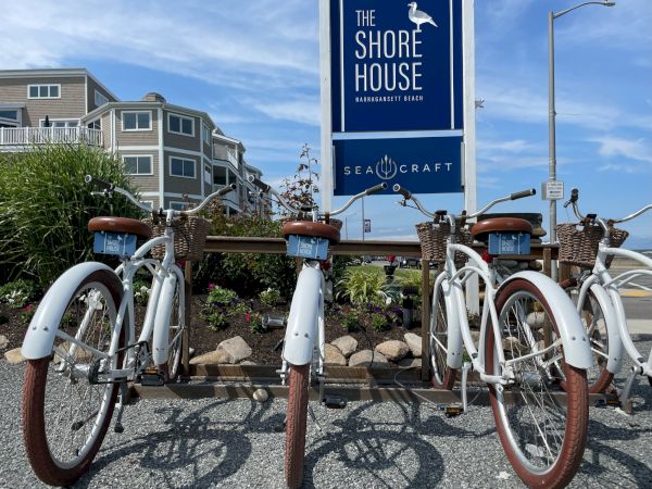 The image shows a row of white bicycles parked in front of a sign that reads "The Shore House" and "Sea Craft."