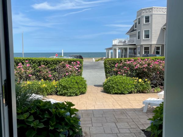 A view from a doorway shows a path leading to a beach, with a charming house and blue sky in the background.