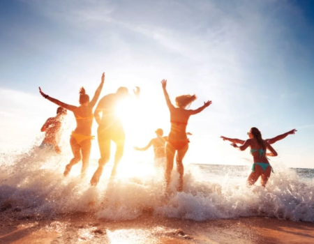 A group of people joyfully splashing in ocean waves at sunset, creating a lively, sunlit silhouette on the beach.