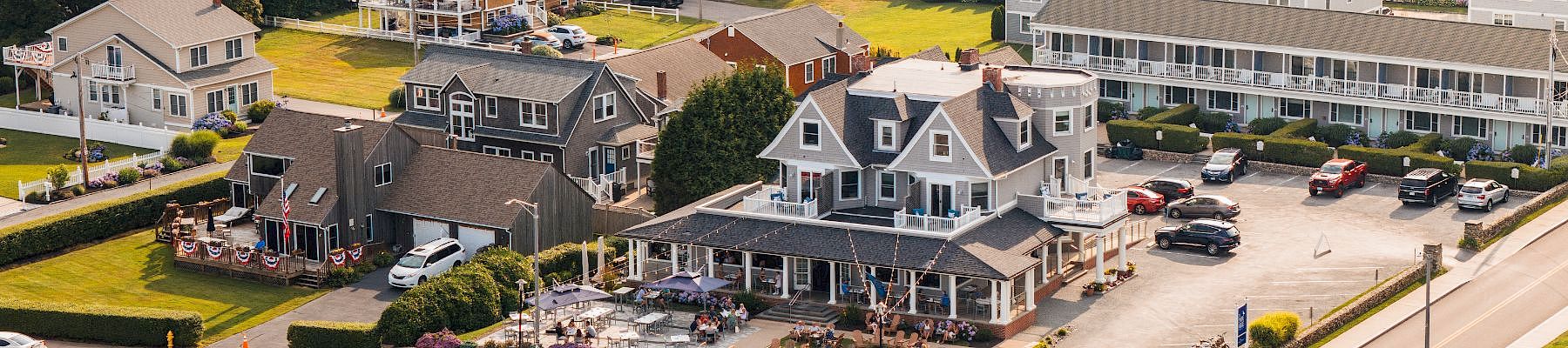 A coastal town with multi-story houses, a beachfront road, and a row of parked cars along a rocky shoreline.passed end.
