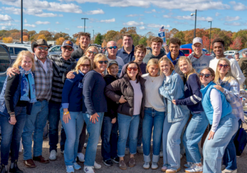 A group of friends posing for a photo outdoors at a park, wearing casual clothes and a few sports caps.